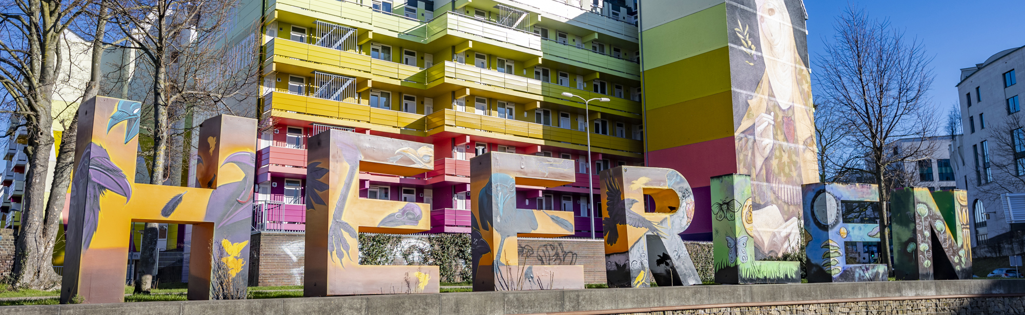 Foto van de grote kleurrijke letters die HEERLEN vormen, met daarachter een kleurrijk appartementencomplex